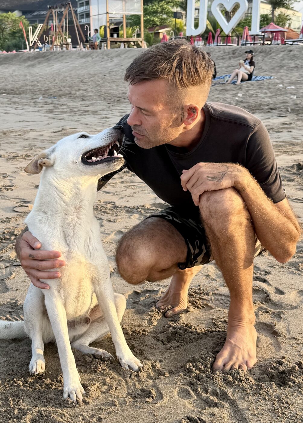 Stephan Mairesse sharing an affectionate moment with a dog on the beach in Bali