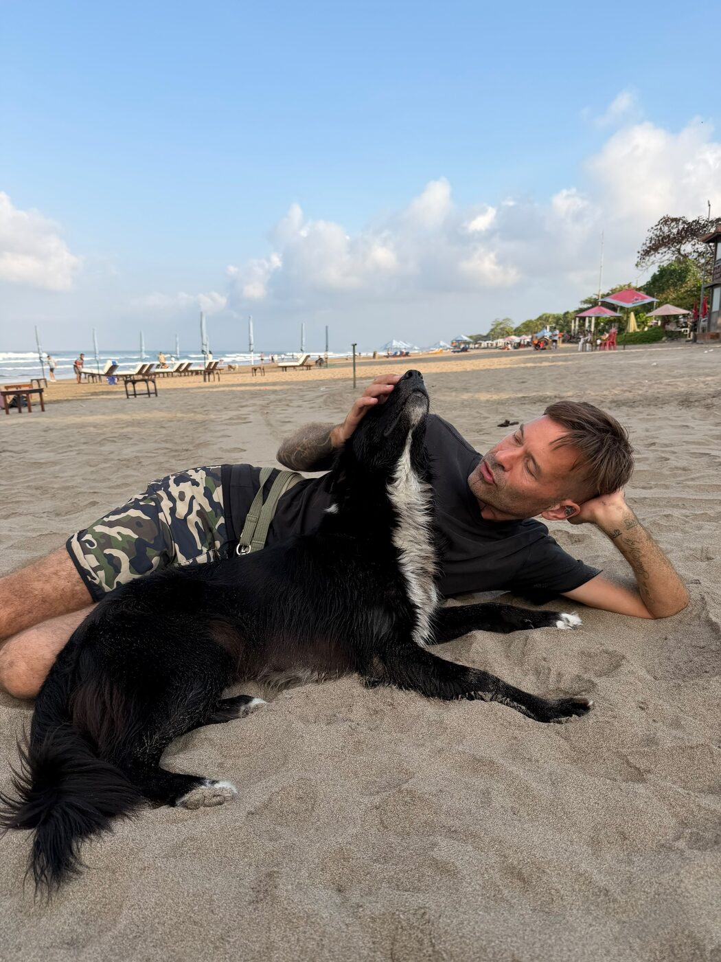 Stephan Mairesse lying on the beach with a black and white dog