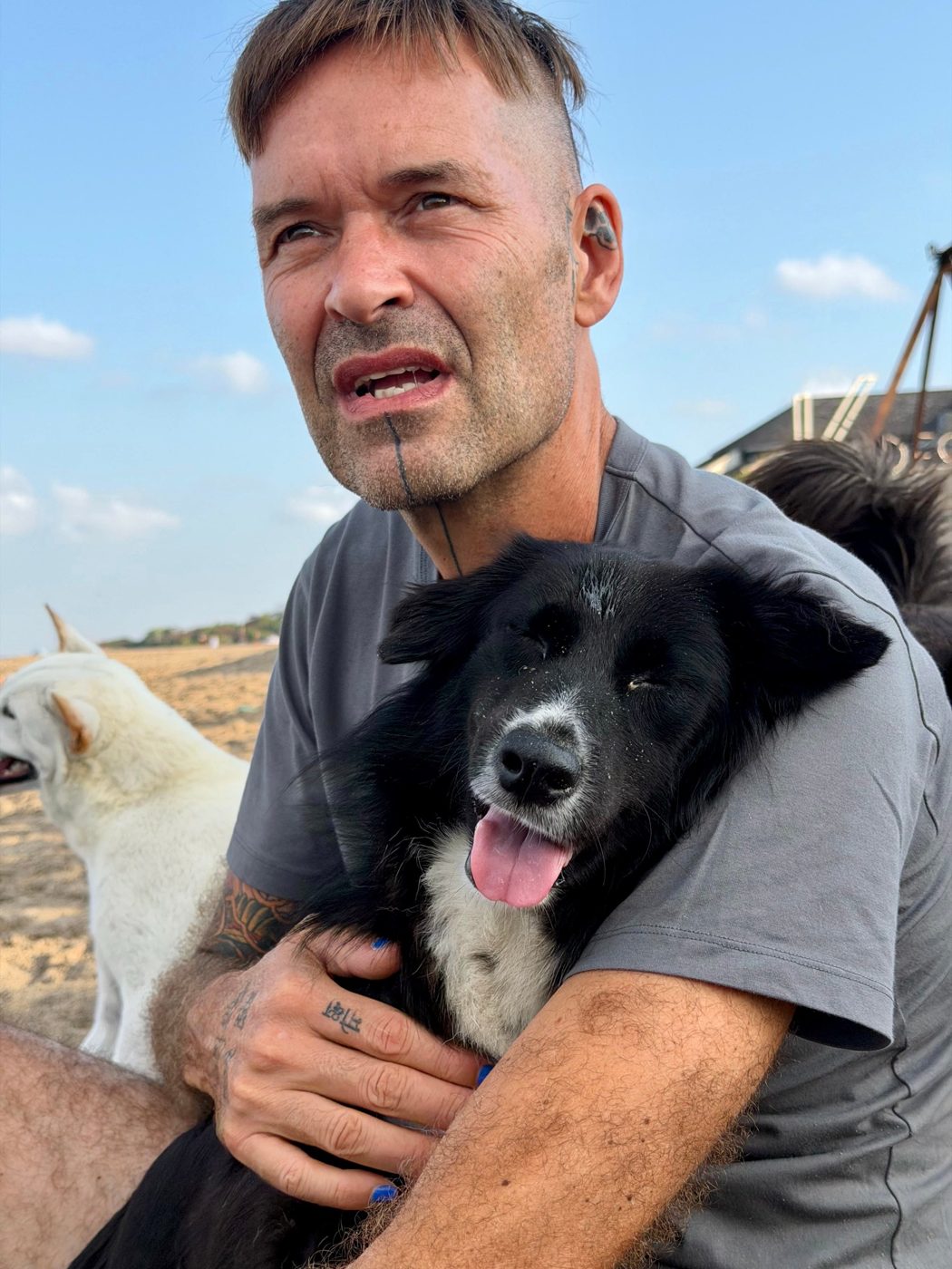 Stephan Mairesse on the beach holding Ruby, a black and white dog, relaxed in his arms with her tongue out